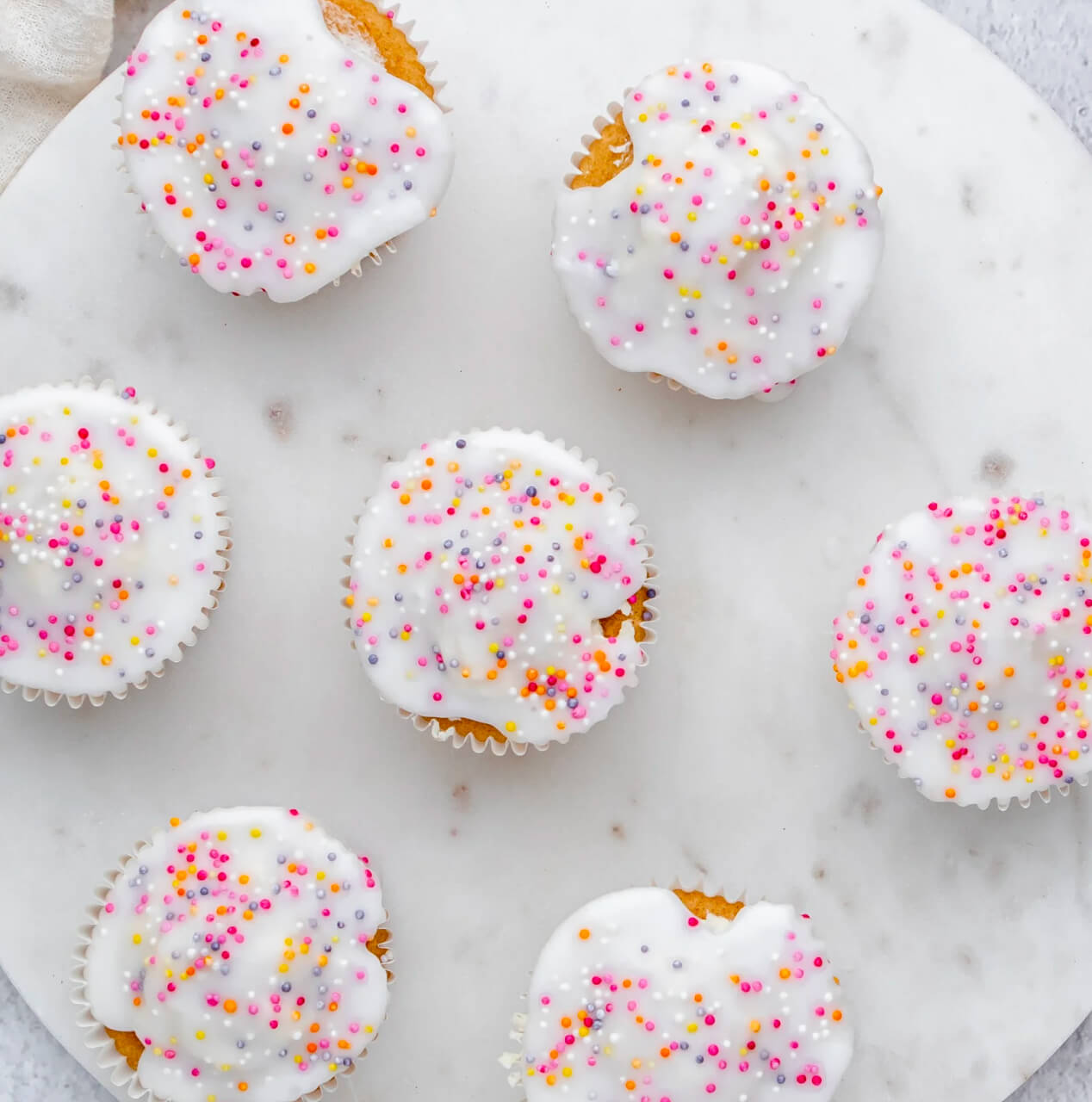 Pretty fairy cakes decorated with white icing and colourful sprinkles.